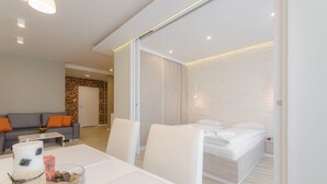 Una habitación de hotel moderna con cama, sofá, mesa de comedor y una pequeña cocina.