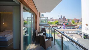 Un balcón con mobiliario de mimbre, una cama y vistas a un puerto deportivo y al paisaje urbano.