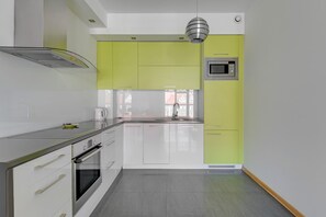 A modern kitchen with white and green cabinets, stainless steel appliances, and a large window.