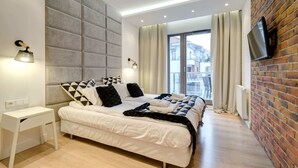Una habitación de hotel moderna con una cama grande, un televisor de pantalla plana montado en una pared de ladrillo y vistas a la ciudad a través de la ventana.