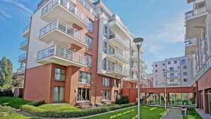 Un edificio residencial moderno de varios pisos, con balcones, una zona exterior cubierta y un césped bien cuidado.