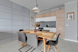 Une cuisine moderne avec des meubles en bois, un four encastré et un coin repas comprenant une table en bois et des chaises grises.