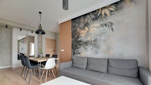 A modern living room with a grey sofa, a white coffee table, and a dining area with chairs and a table. - Tasteful Apartment in the Center | Pool, Sauna and Gym (Gdańsk)