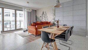 A modern living room with a sofa, dining table, chairs, and a large window. - Tasteful Apartment in the Center | Pool, Sauna and Gym (Gdańsk)