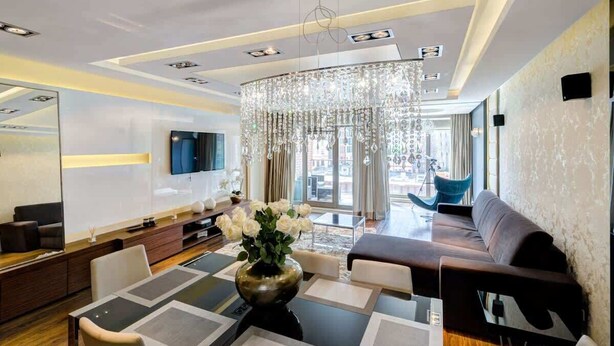 Une chambre d’hôtel moderne dotée d’un coin repas, d’un canapé, d’une télévision et d’un lustre.