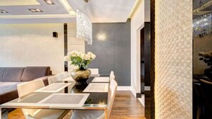 Un espace repas moderne avec une table en verre, des chaises blanches, un vase rempli de fleurs et un mur d’accent de couleur grise.