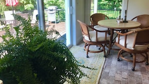 A covered patio with wicker chairs and a table, a potted plant, and a red umbrella.