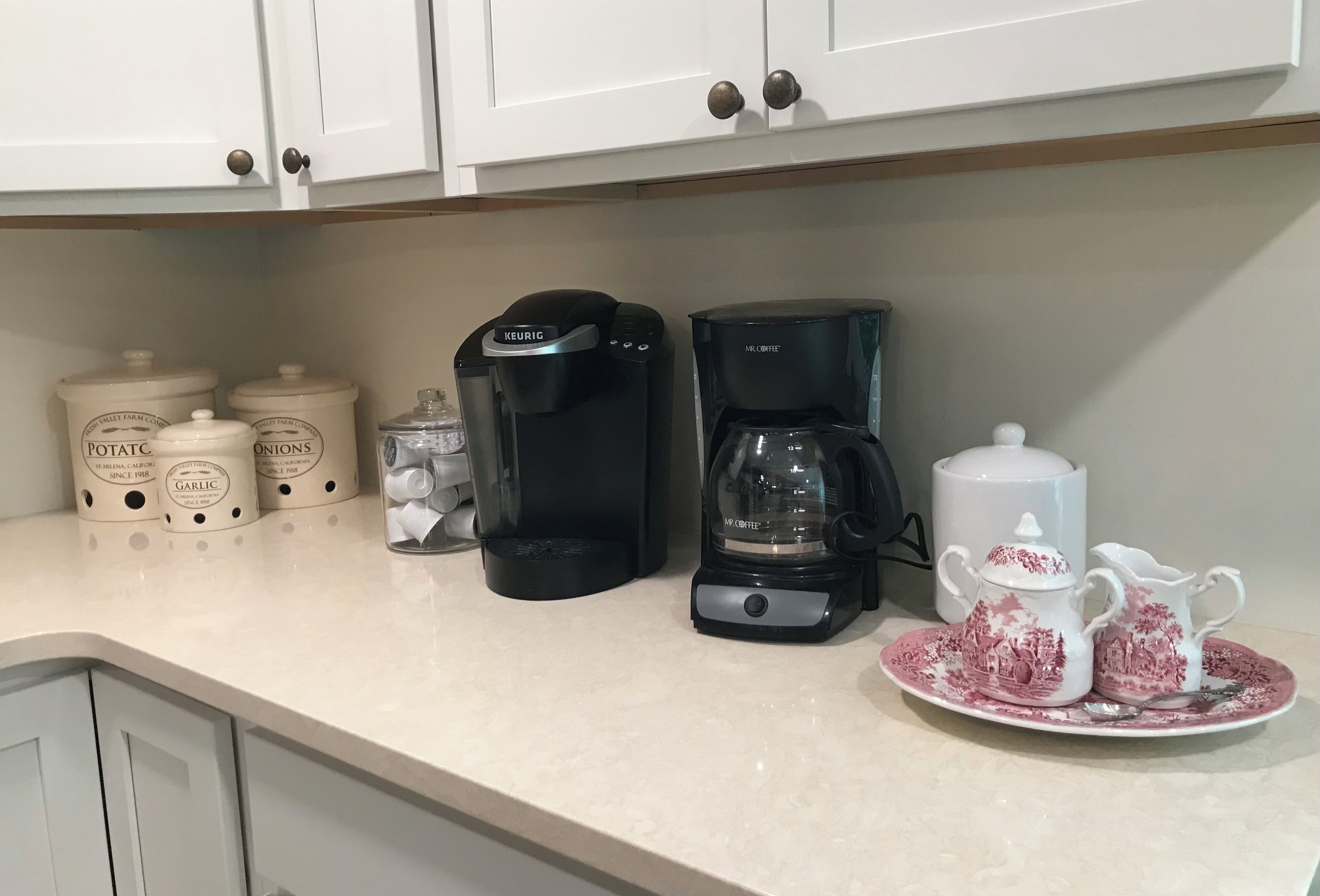 A kitchen counter with two coffee makers, a set of condiment containers, and a tea set.
