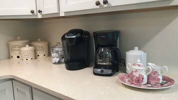 A kitchen counter with two coffee makers, a set of condiment containers, and a tea set.