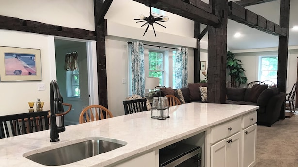 A kitchen with a large island, white cabinetry, and a black microwave. There is a window with curtains and a plant in the background.