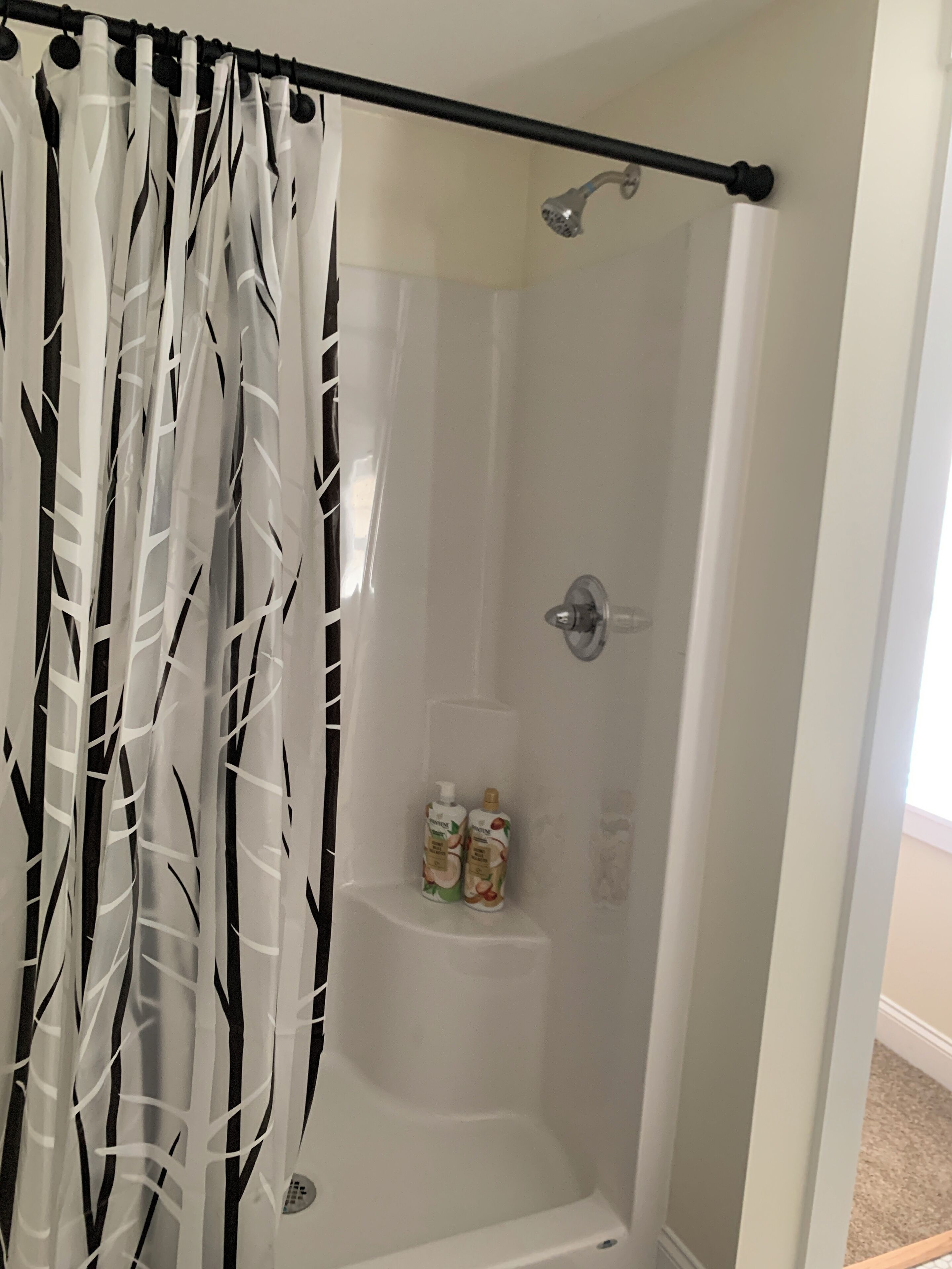 Eine Dusche mit schwarzem Vorhang, einer Handbrause und zwei Shampoo-Flaschen an der Wand.