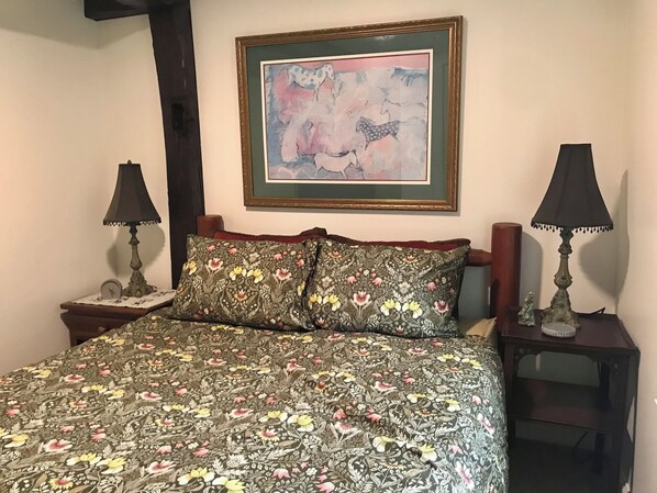 Un dormitorio con colcha estampada, un cuadro abstracto enmarcado, dos lámparas de noche y una pequeña estatua sobre una mesita de noche.