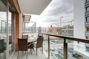 A balcony with wicker chairs and a table, overlooking a cityscape with historic buildings and construction cranes.