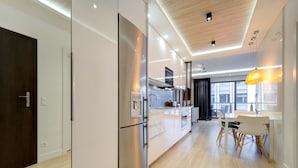 Una cocina moderna con electrodomésticos de acero inoxidable, un comedor con sillas blancas y un amplio ventanal que proporciona luz natural.
