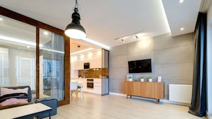 Una sala de estar moderna con un sofá, una mesa de comedor, una cocina al fondo y un televisor montado en la pared.