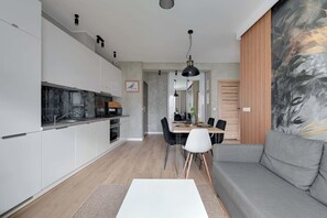 A modern kitchen with white cabinets, a dining area with a table and chairs, and a gray sofa.