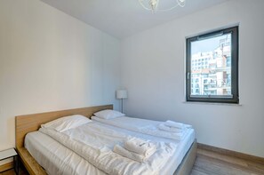 Habitación de hotel moderna y luminosa con una cama grande, una lámpara de noche y una ventana con vistas a la ciudad.