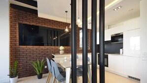 Een moderne keuken met witte kasten, een zwarte oven en een grote flatscreen televisie bevestigd aan een bakstenen muur.