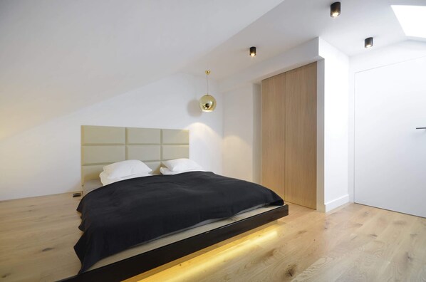 A modern bedroom with a bed, a headboard, a wardrobe, and a skylight.