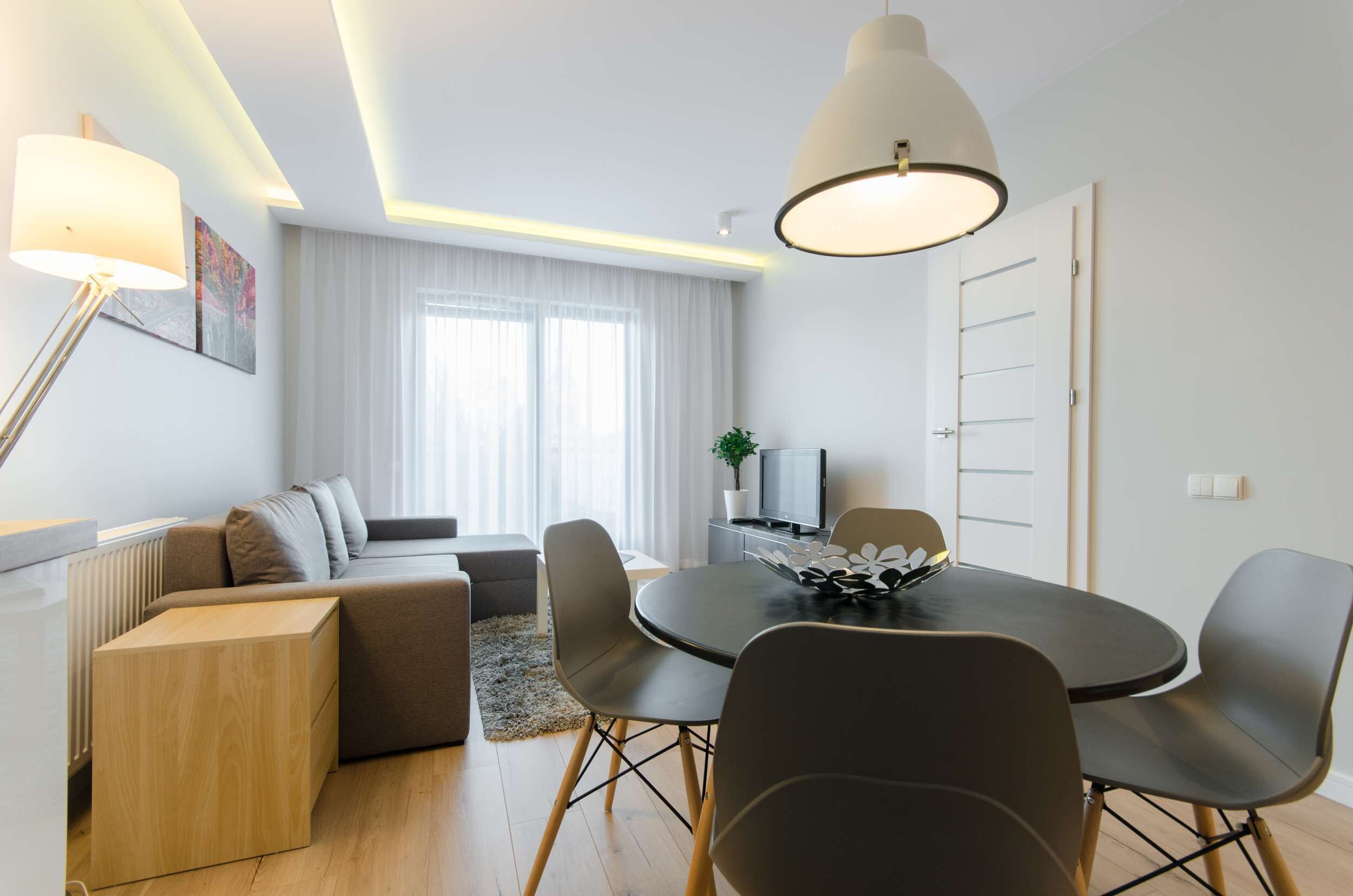 Ein modernes Wohnzimmer mit einer Couch, einem Esstisch mit Stühlen, einem Fernseher und einer Pflanze.