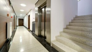 A hotel corridor with a staircase, an elevator, and a tiled floor.