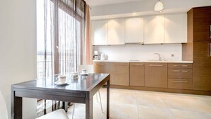 A modern kitchen with a dining table, a coffee machine, and a large window with curtains.