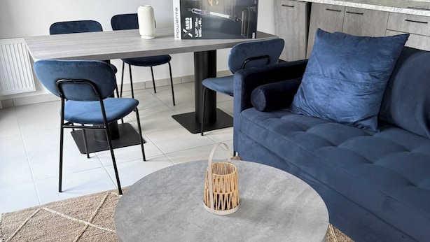 A modern living room with a round coffee table, blue sofa, and dining area with chairs.