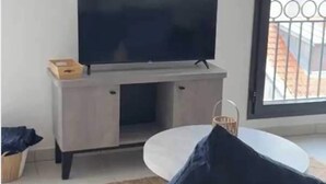 A modern living room with a flat-screen TV on a wooden cabinet, a round white coffee table, and a dark blue sofa.