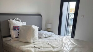 A hotel room with a bed covered in plastic, a nightstand with a lamp, and a window with a view of buildings.