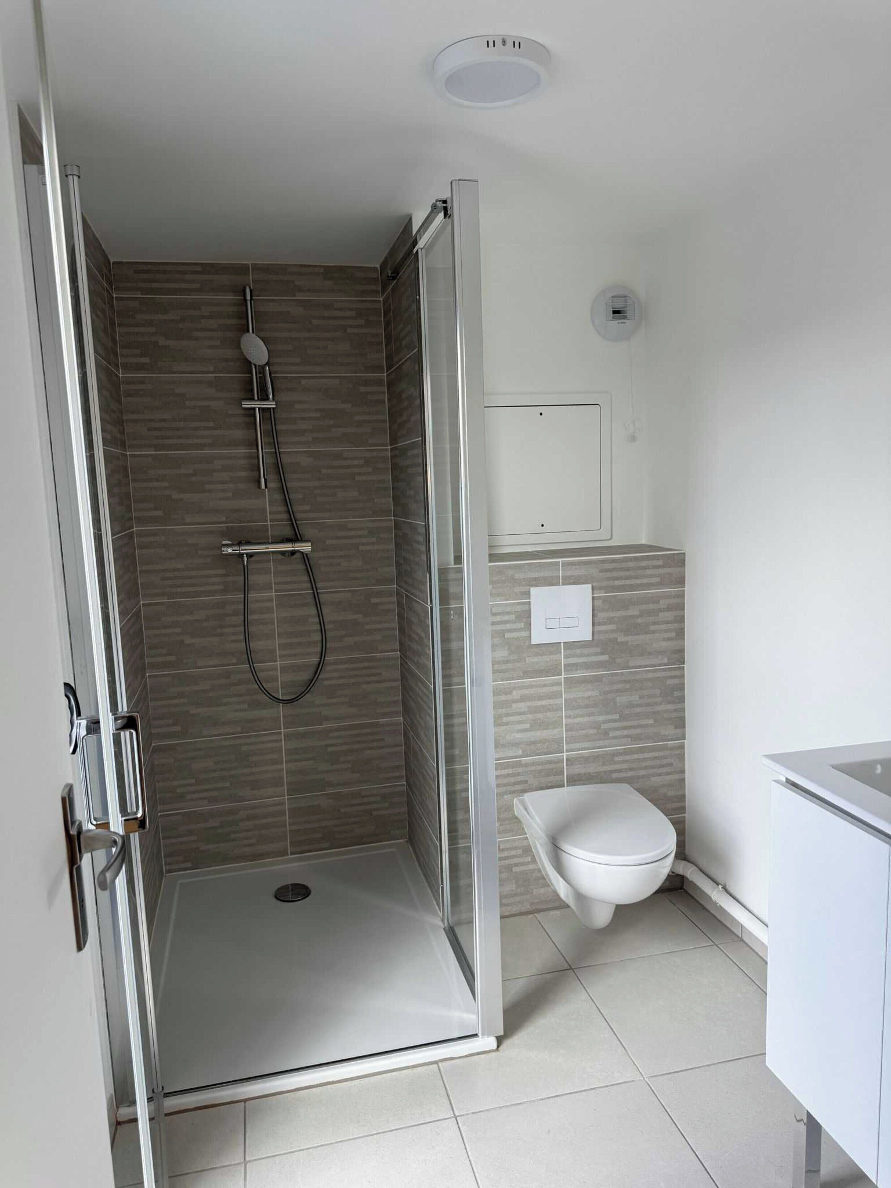 A modern bathroom with a glass-enclosed shower, a toilet, and a sink.