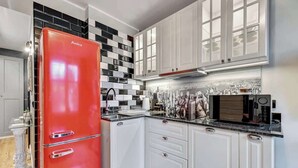 A kitchen with white cabinets, a red refrigerator, a microwave, and a tiled backsplash.