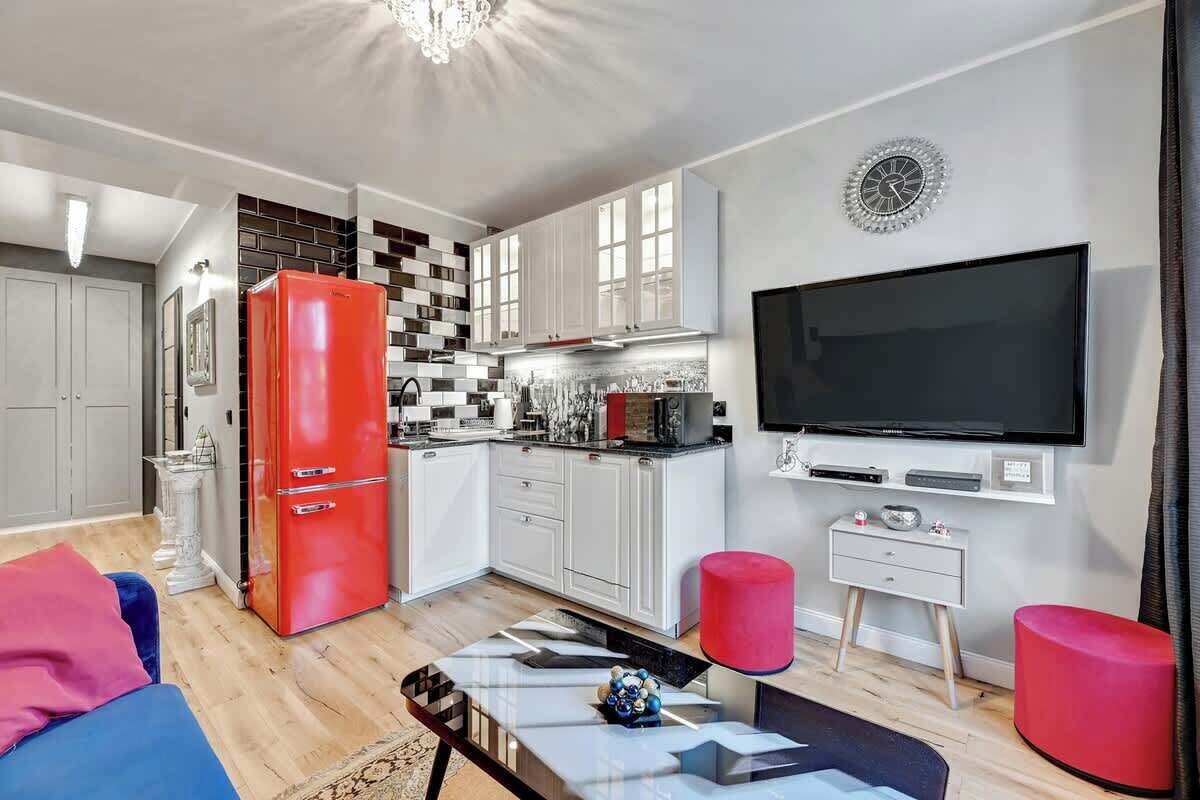 A modern kitchen with white cabinets, a red refrigerator, and a large flat-screen TV.