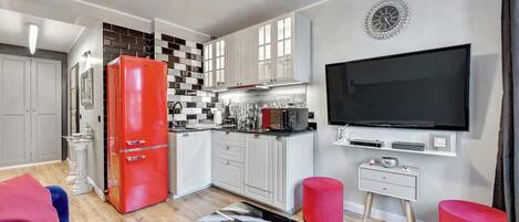 A modern kitchen with white cabinets, a red refrigerator, and a large flat-screen TV.