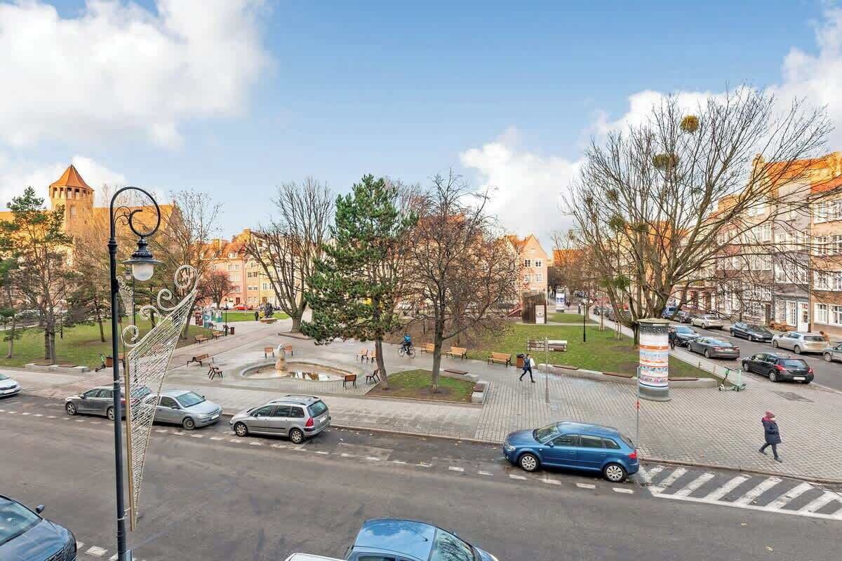 Vista de la calle con coches, peatones y edificios, incluyendo una estructura tipo torre al fondo.