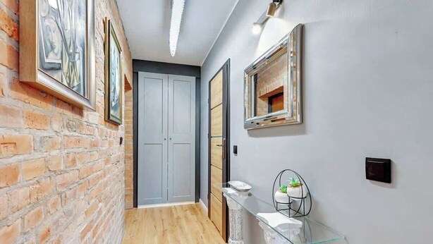 A hallway with a brick wall, a glass shelf with a plant, and a door with a mirror.