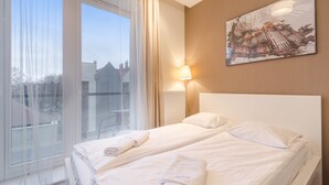 A hotel room with two beds, a large window with curtains, a painting on the wall, and a lamp. - Modern Studio in the Center | Balcony and Bathtub (Gdańsk)