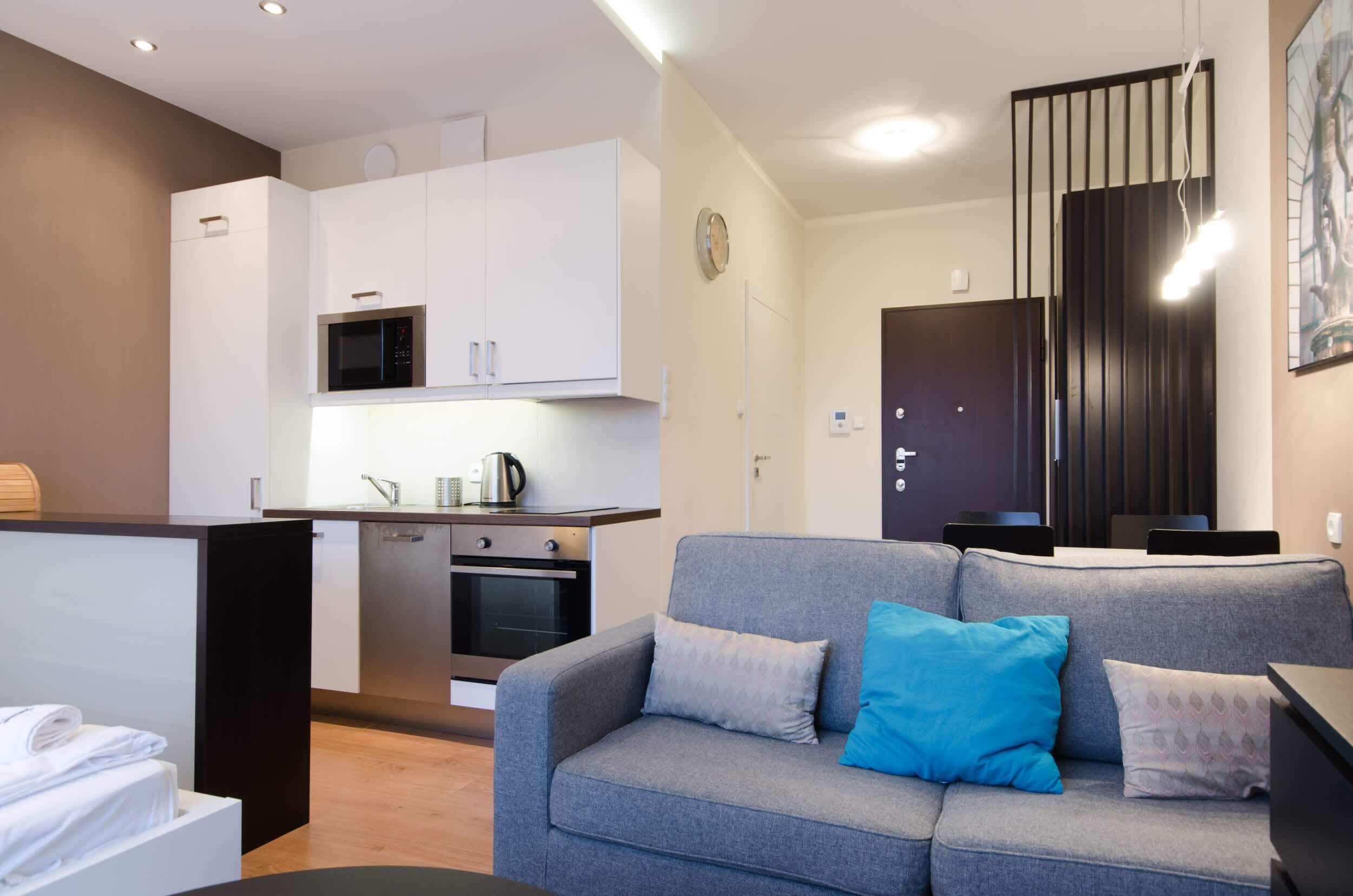 Een moderne woonkamer met een grijze bank, een salontafel en een keuken met witte kasten en een magnetron.
