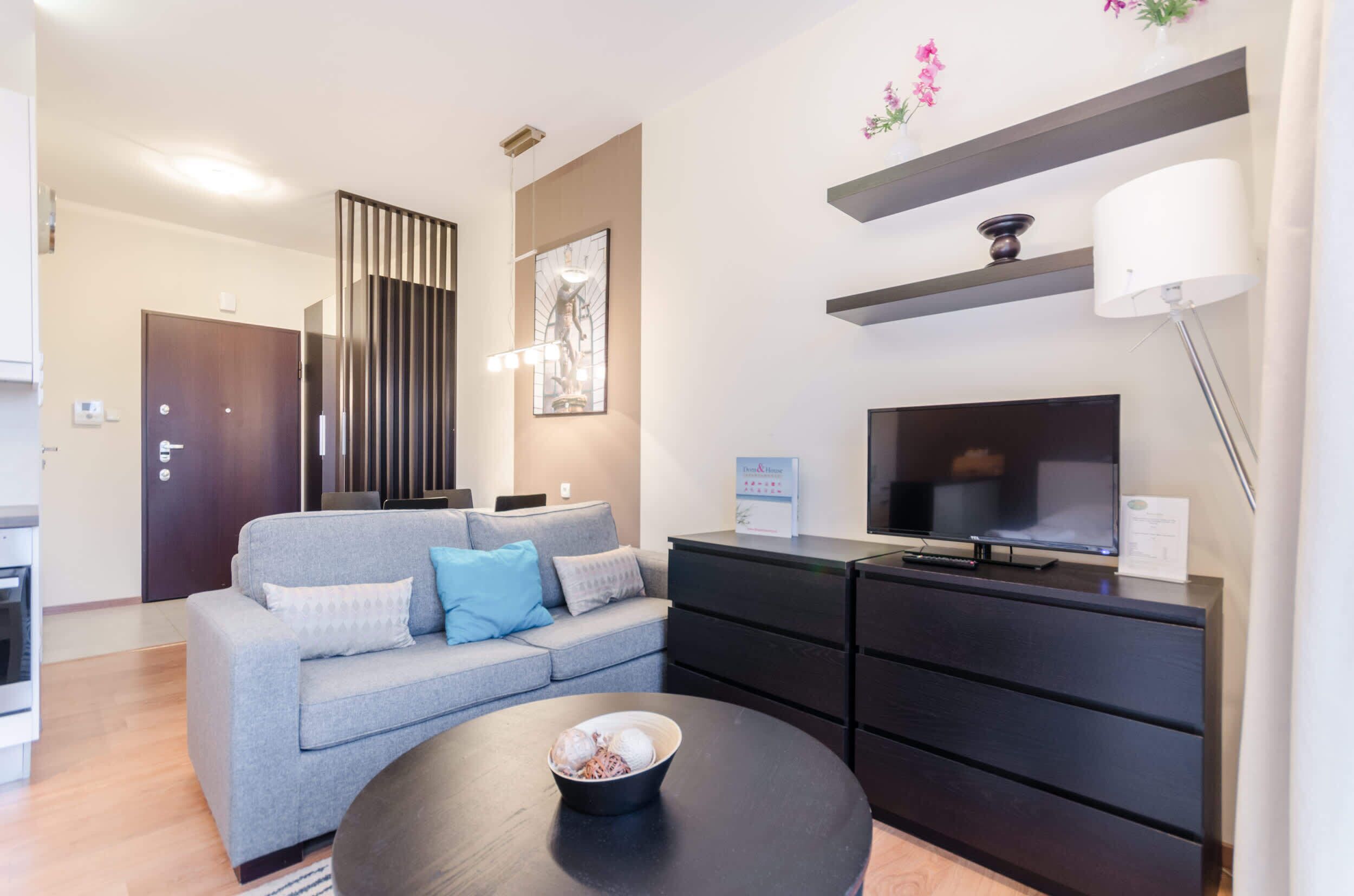 Una sala de estar moderna con un sofá gris, almacenamiento negro, un televisor y un cuenco sobre una mesa de centro.
