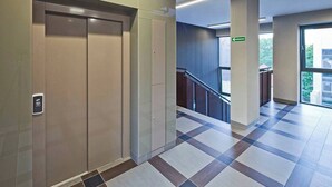 An interior corridor with a checkered floor, a staircase, and a glass elevator. - Modern Studio in the Center | Balcony and Bathtub (Gdańsk)