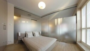 A bedroom with a bed, bedside tables, a wall-mounted light, and a window with blinds.
