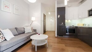 Un salon moderne avec un canapé gris, une table ronde blanche et un coin cuisine doté de meubles sombres et d’un four à micro-ondes.