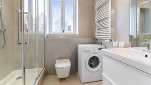 Une salle de bain moderne avec une douche à parois de verre, un lave-linge et des toilettes.