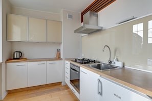 A modern kitchen with white cabinets, a stainless steel sink, a built-in oven, and a range hood.
