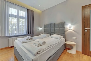 A serene space with a large double bed, soft bedding, and warm lighting, complemented by wooden floors and neutral decor.