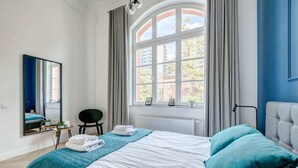 Une chambre à coucher moderne avec un grand lit, une chaise, une petite table et une fenêtre avec des rideaux.
