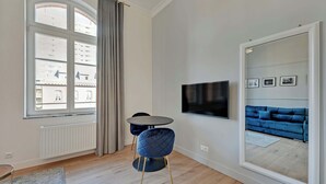 A modern living room with a large window, a round table, a blue sofa, and a TV mounted on the wall. - Tasteful Studio | Gym in Building, Acceptance of Pets (Gdańsk)