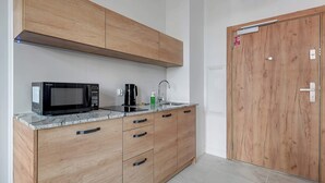 A modern kitchen with wooden cabinets, a microwave, a coffee maker, and a sink. - Tasteful Studio | Gym in Building, Acceptance of Pets (Gdańsk)