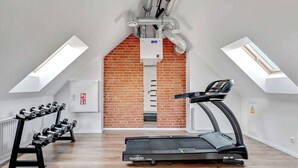 A gym with a treadmill, dumbbells, and a brick wall. - Tasteful Studio | Gym in Building, Acceptance of Pets (Gdańsk)
