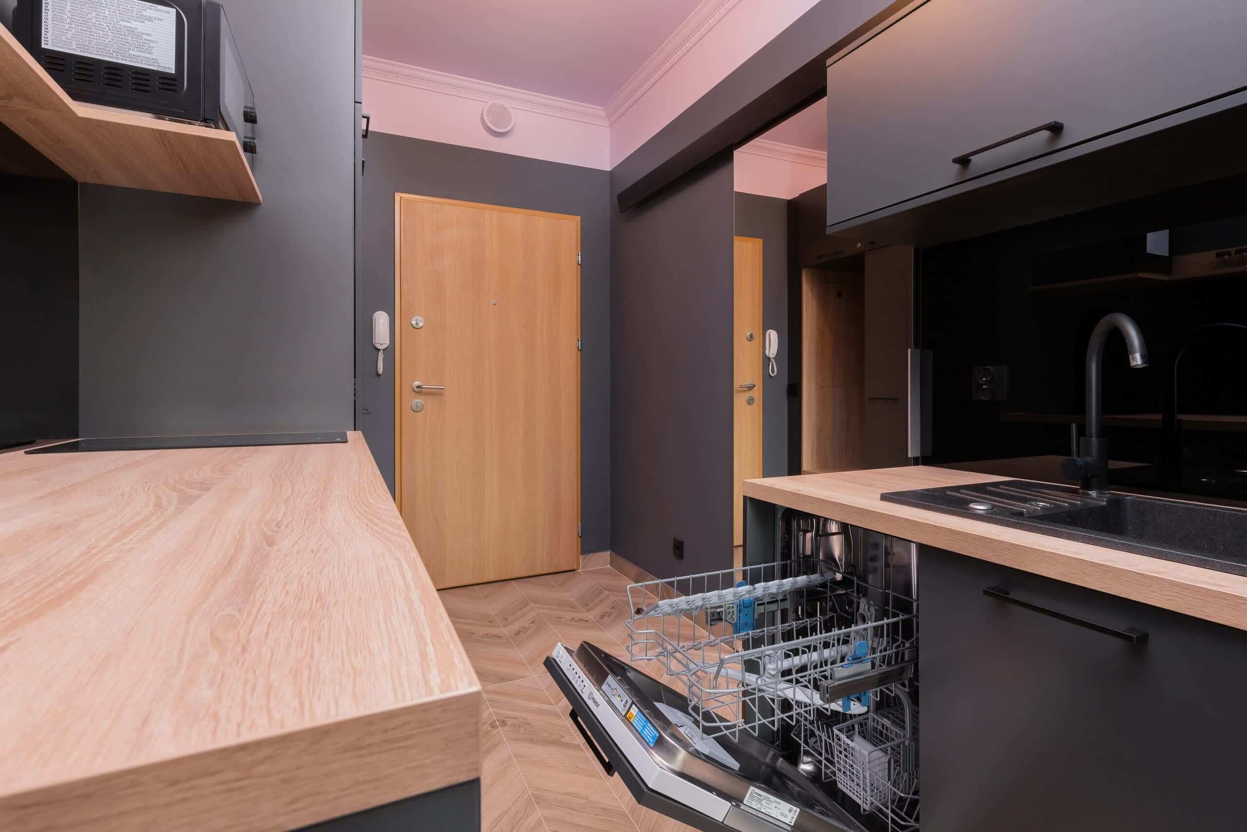 Una cocina compacta con lavavajillas, encimera de madera y pared oscura.