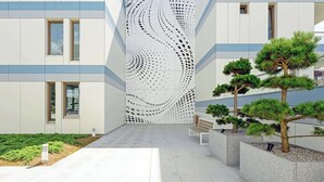 A modern building with a unique perforated wall design, outdoor seating, and well-maintained landscaping.
